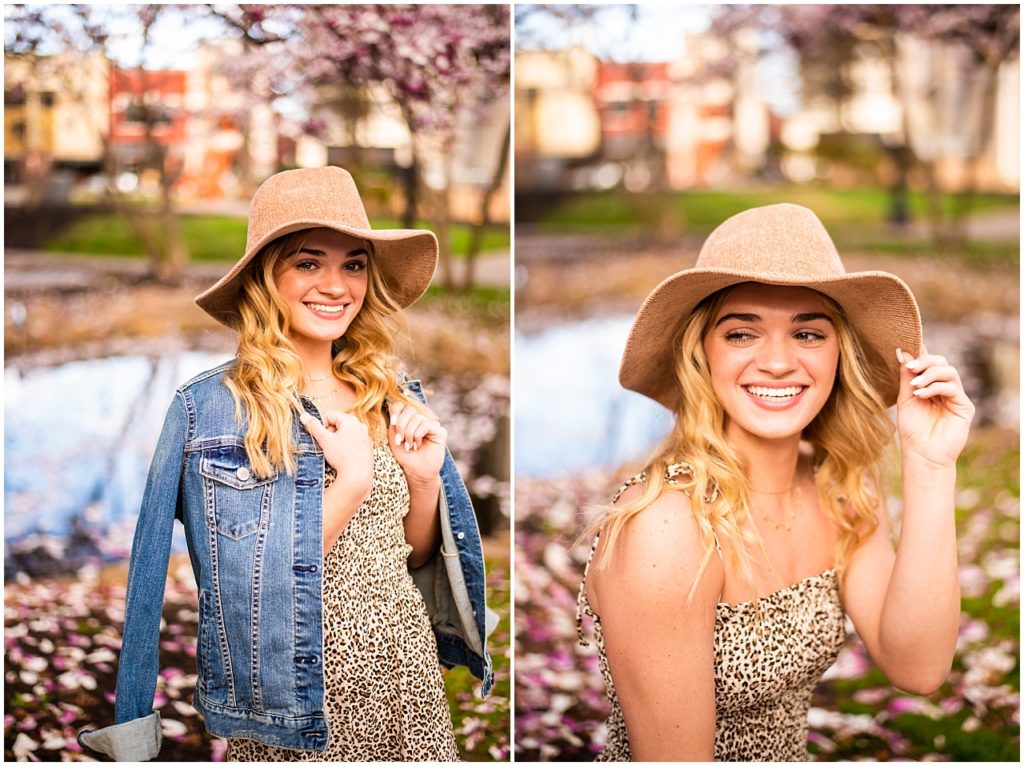 Blonde girl wearing jean jacket and leopard jumpsuit and brown hat in park with flower petals on ground.